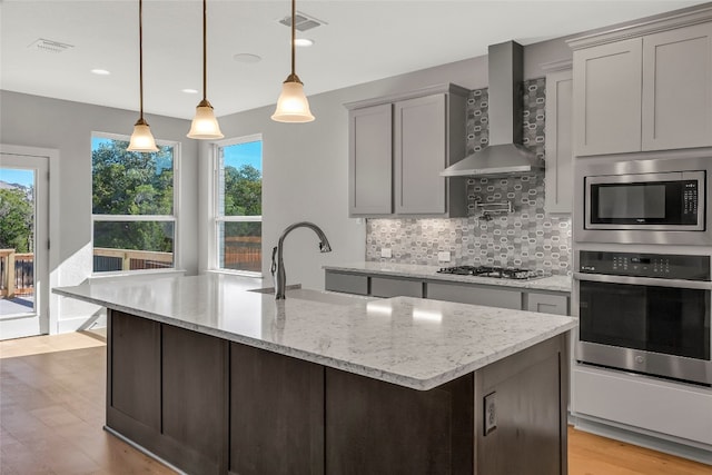 kitchen with wall chimney range hood, a wealth of natural light, stainless steel appliances, and backsplash