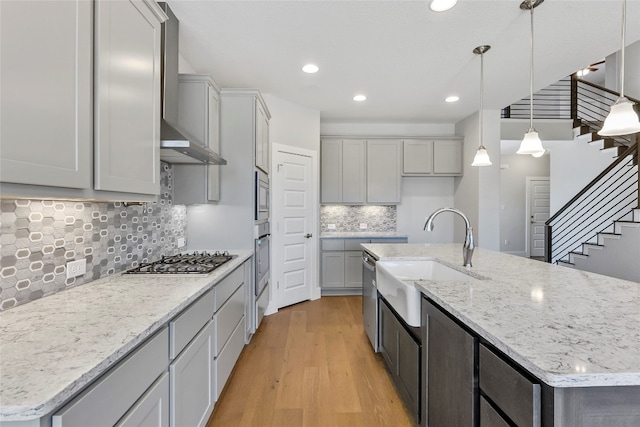 kitchen featuring light hardwood / wood-style floors, a center island with sink, appliances with stainless steel finishes, decorative light fixtures, and backsplash