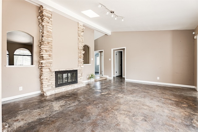 unfurnished living room featuring track lighting, a stone fireplace, vaulted ceiling with beams, and concrete floors