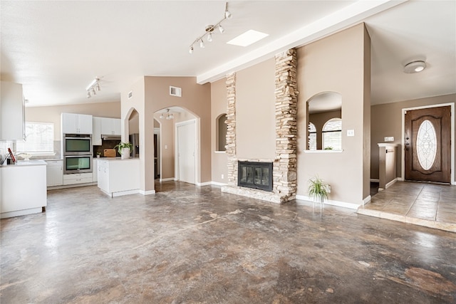 unfurnished living room featuring a wealth of natural light, lofted ceiling with beams, track lighting, and a stone fireplace