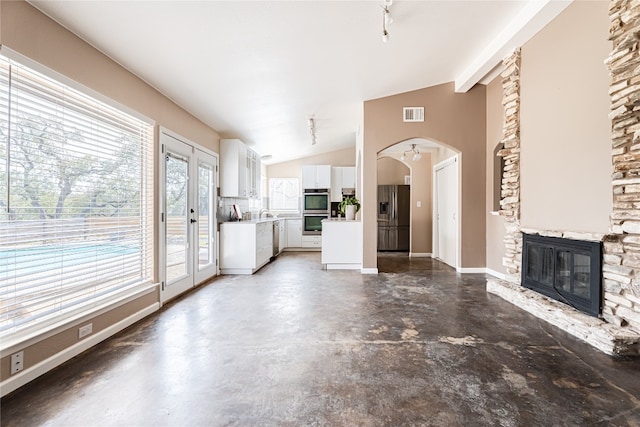 unfurnished living room featuring concrete floors, french doors, a fireplace, and lofted ceiling