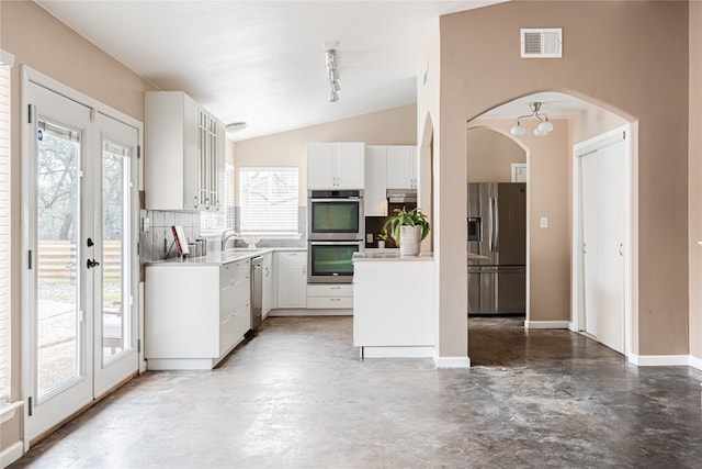 kitchen with vaulted ceiling, stainless steel appliances, tasteful backsplash, white cabinetry, and track lighting