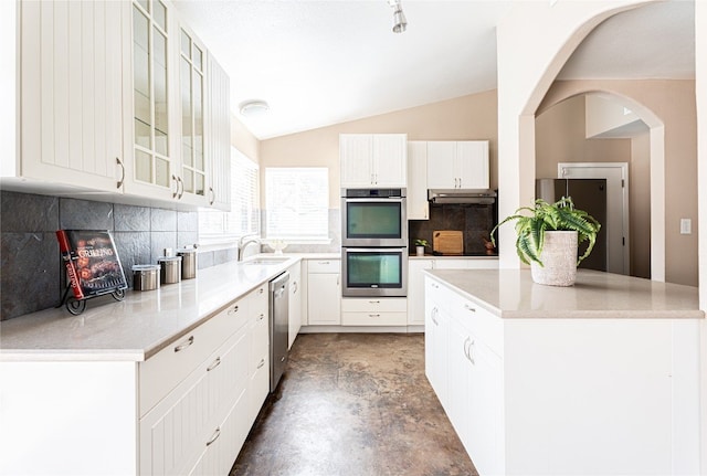 kitchen featuring stainless steel appliances, tasteful backsplash, white cabinetry, concrete floors, and lofted ceiling