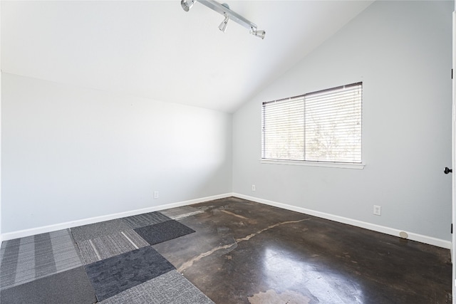 empty room with concrete flooring, vaulted ceiling, and rail lighting