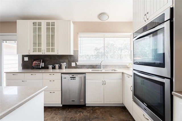 kitchen with dark tile floors, tasteful backsplash, white cabinetry, appliances with stainless steel finishes, and sink