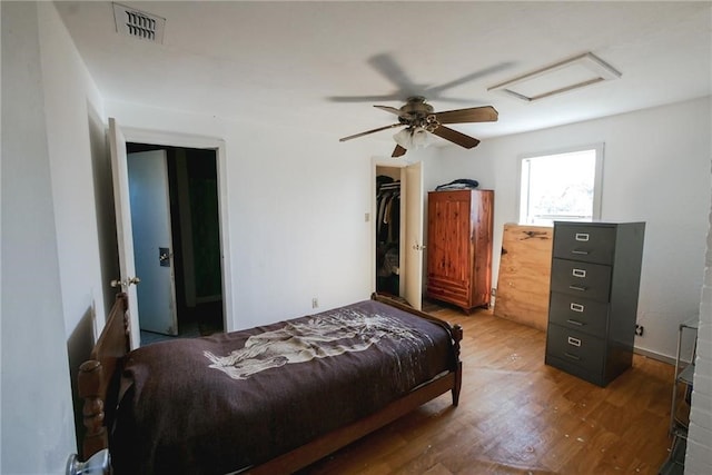 bedroom with a spacious closet, a closet, wood-type flooring, and ceiling fan