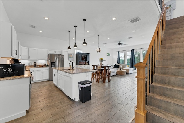 kitchen with light stone counters, a center island with sink, white cabinets, and decorative light fixtures