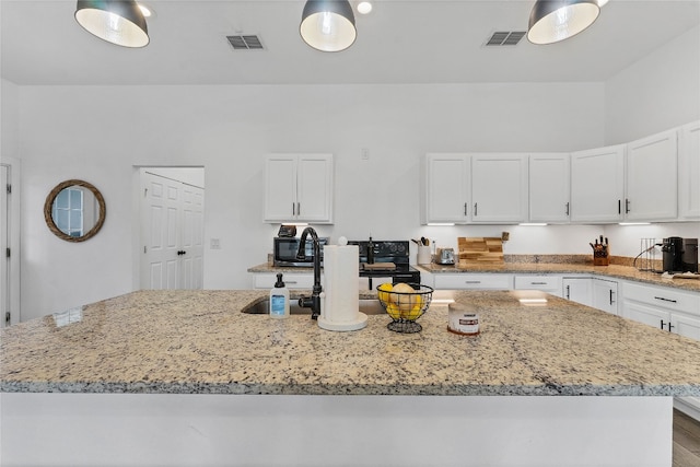 kitchen featuring light stone countertops, hardwood / wood-style floors, a kitchen island with sink, and white cabinetry