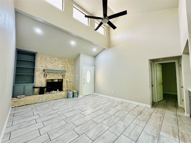 unfurnished living room with light tile patterned floors, built in features, ceiling fan, a fireplace, and a towering ceiling