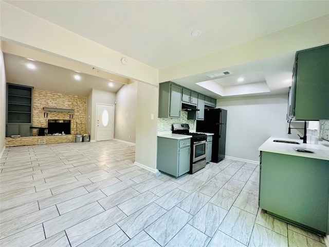 kitchen featuring a stone fireplace, stainless steel range with gas stovetop, tasteful backsplash, black fridge, and light tile patterned floors