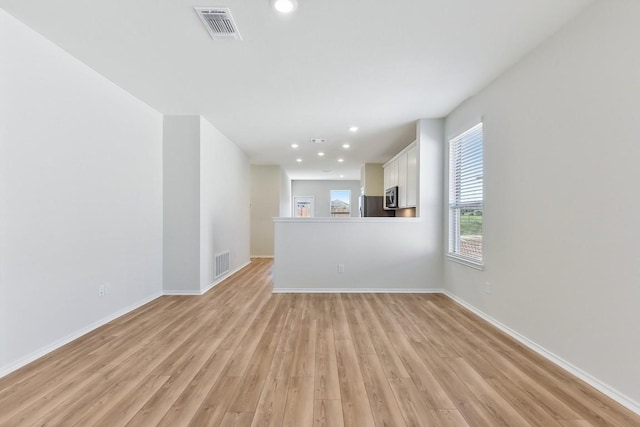 unfurnished living room with light wood-type flooring, visible vents, and baseboards