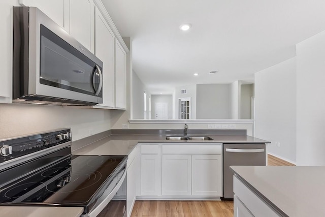 kitchen with light wood finished floors, white cabinets, stainless steel appliances, a sink, and recessed lighting