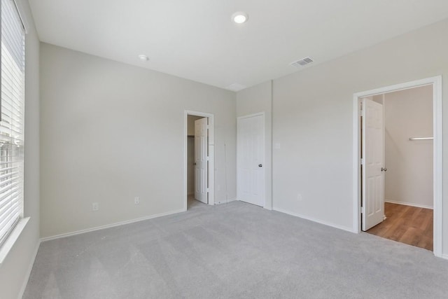 unfurnished bedroom with carpet, visible vents, and a walk in closet