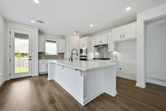 kitchen featuring stainless steel appliances, dark hardwood / wood-style floors, white cabinets, and a kitchen island with sink