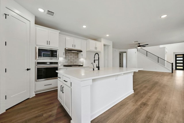 kitchen featuring appliances with stainless steel finishes, white cabinetry, dark hardwood / wood-style floors, ceiling fan, and a center island with sink