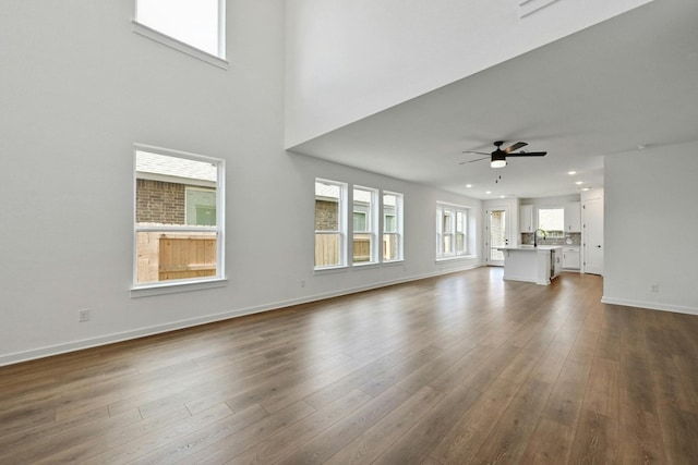 unfurnished living room with a high ceiling, ceiling fan, hardwood / wood-style flooring, and sink