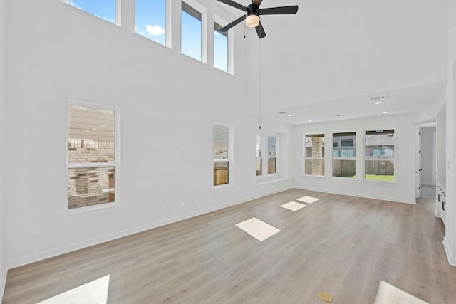 unfurnished living room featuring ceiling fan, a towering ceiling, and light hardwood / wood-style flooring