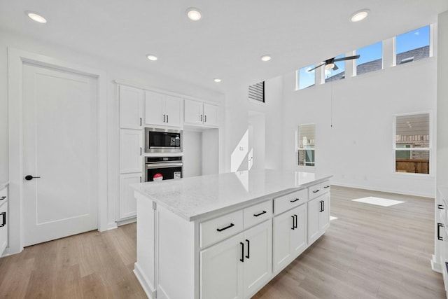 kitchen featuring light stone counters, a kitchen island, white cabinetry, appliances with stainless steel finishes, and light hardwood / wood-style floors