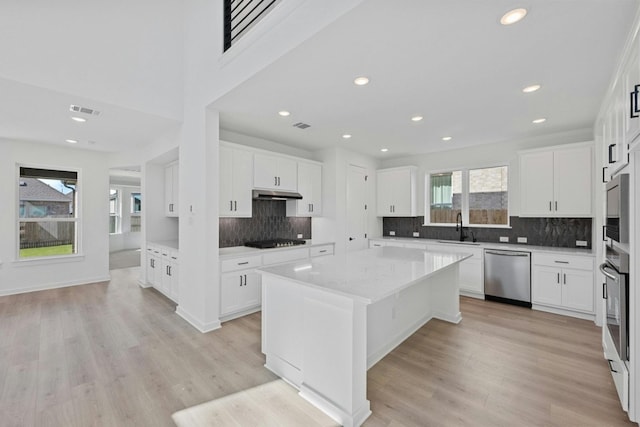 kitchen with a kitchen island, light hardwood / wood-style flooring, stainless steel dishwasher, and white cabinetry