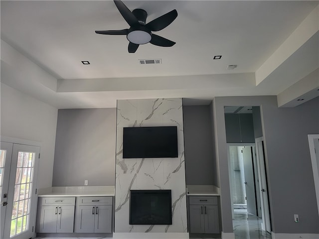 unfurnished living room featuring ceiling fan, a tray ceiling, and light tile floors