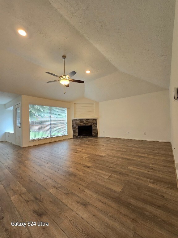 unfurnished living room with a textured ceiling, dark hardwood / wood-style floors, a stone fireplace, lofted ceiling, and ceiling fan