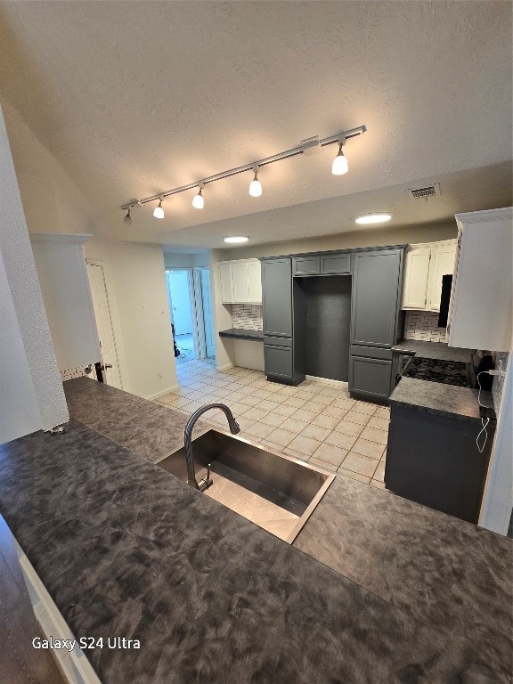 kitchen featuring tasteful backsplash, rail lighting, a textured ceiling, sink, and light tile patterned flooring