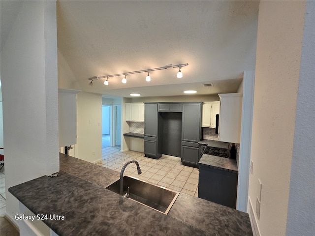 kitchen featuring tasteful backsplash, rail lighting, light tile patterned floors, sink, and gray cabinetry