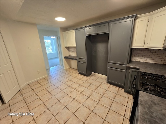 kitchen featuring black gas range, light tile patterned floors, backsplash, and white cabinets