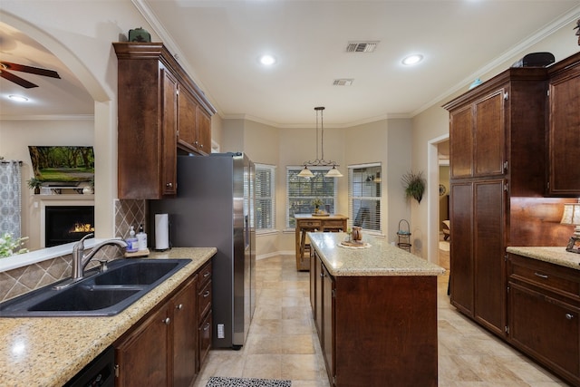 kitchen with light stone counters, sink, crown molding, decorative light fixtures, and a center island