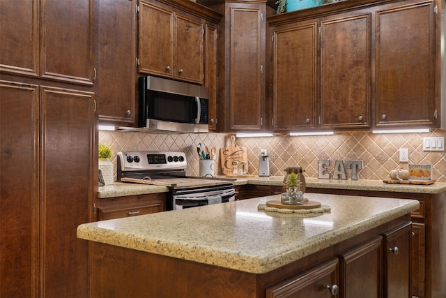 kitchen featuring backsplash, stainless steel appliances, light stone countertops, and a kitchen island