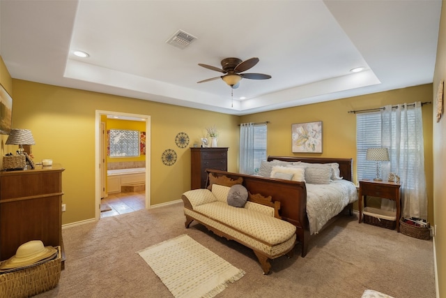 carpeted bedroom with ensuite bathroom, a tray ceiling, and ceiling fan