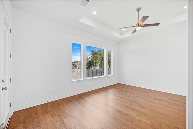 unfurnished room with ceiling fan, light wood-type flooring, and a tray ceiling