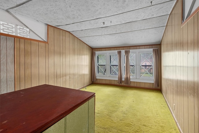 interior space featuring carpet, wooden walls, a textured ceiling, and lofted ceiling