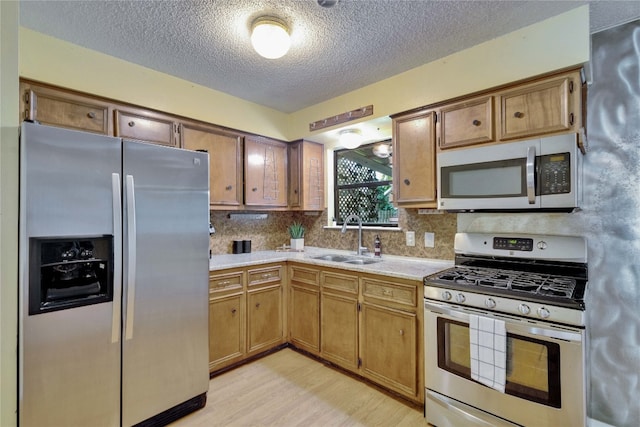 kitchen with a textured ceiling, sink, light hardwood / wood-style flooring, backsplash, and appliances with stainless steel finishes