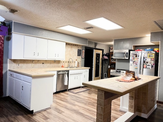 kitchen featuring white cabinets, backsplash, appliances with stainless steel finishes, light hardwood / wood-style flooring, and sink