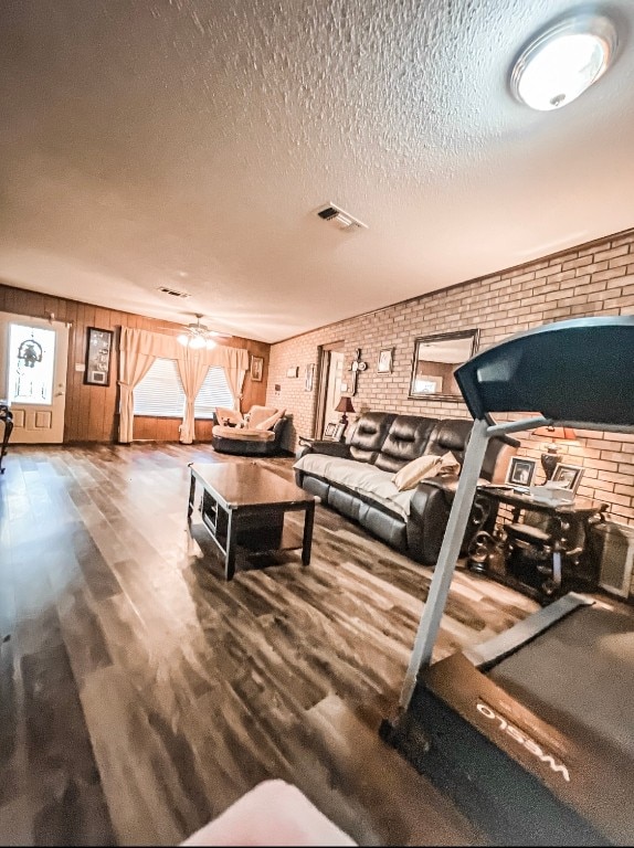 workout area featuring brick wall, a textured ceiling, wood-type flooring, and ceiling fan