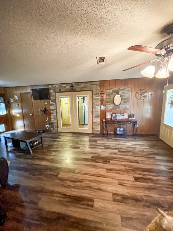 living room featuring french doors, a textured ceiling, wood-type flooring, and wooden walls