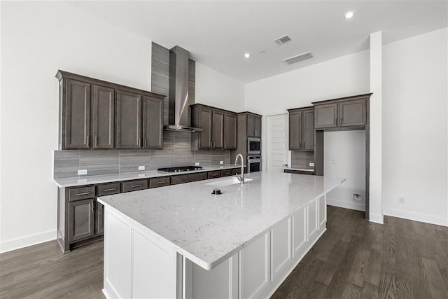 kitchen featuring sink, wall chimney exhaust hood, an island with sink, appliances with stainless steel finishes, and dark hardwood / wood-style flooring