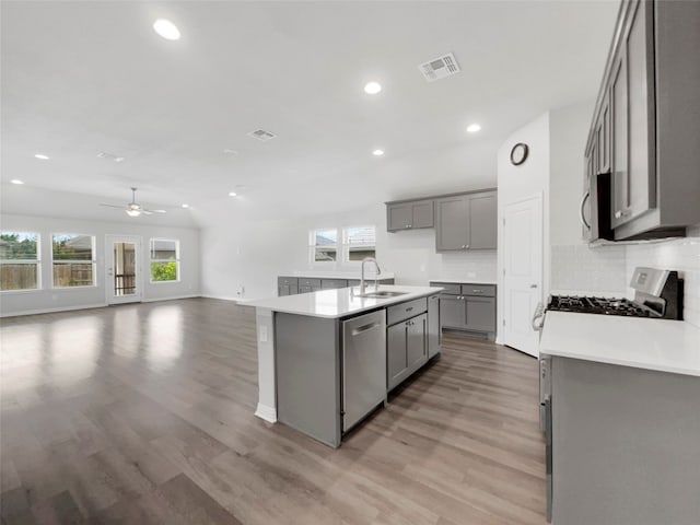 kitchen with ceiling fan, light hardwood / wood-style floors, stainless steel appliances, sink, and a kitchen island with sink