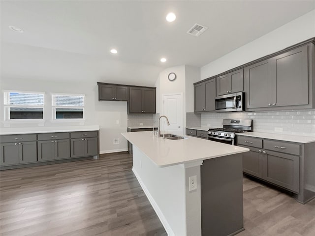 kitchen featuring wood-type flooring, appliances with stainless steel finishes, sink, and a kitchen island with sink