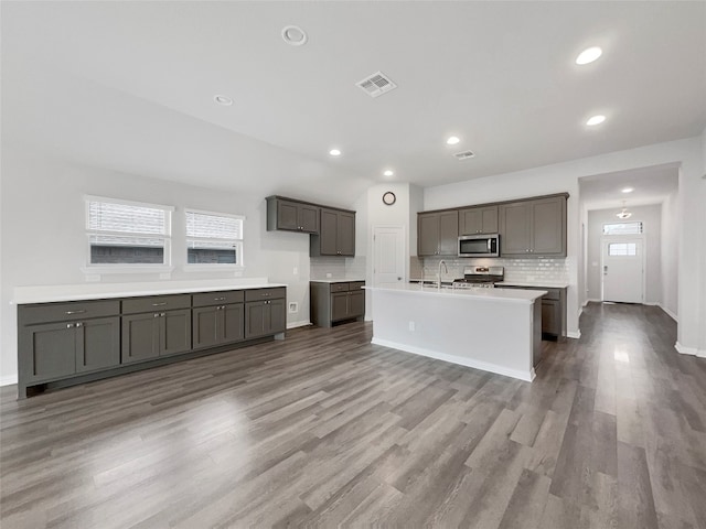 kitchen with backsplash, range, an island with sink, wood-type flooring, and sink