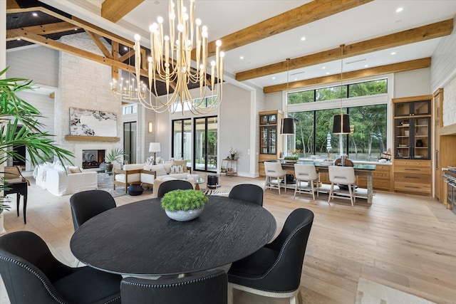 dining area featuring a fireplace, an inviting chandelier, light hardwood / wood-style floors, and beamed ceiling