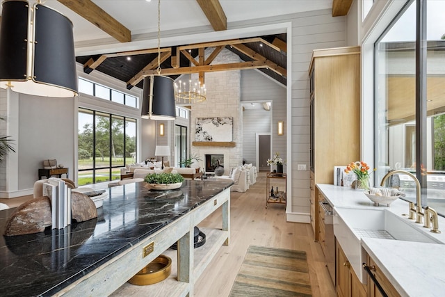 kitchen with decorative light fixtures, light hardwood / wood-style floors, beam ceiling, a fireplace, and sink