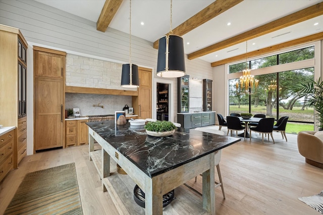 kitchen featuring light wood-type flooring, a center island, pendant lighting, beam ceiling, and an inviting chandelier