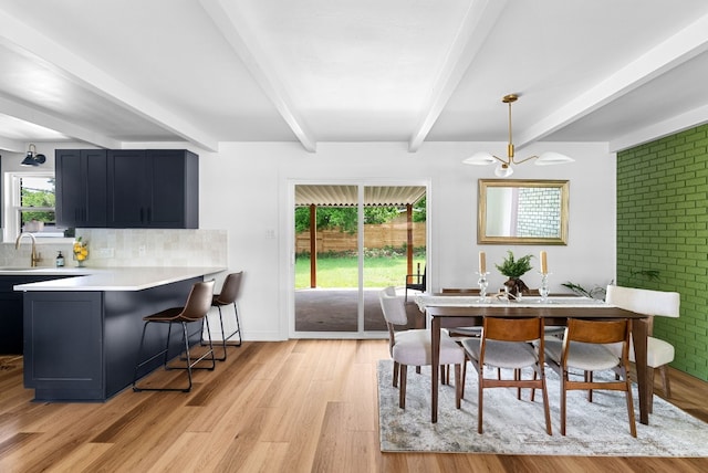 dining room with a notable chandelier, beamed ceiling, sink, and light hardwood / wood-style floors