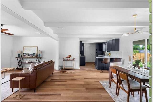 living room featuring beam ceiling, light hardwood / wood-style floors, and a chandelier