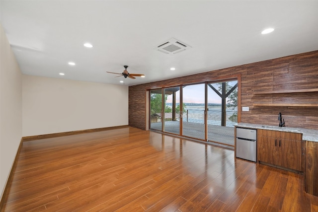 spare room featuring ceiling fan, sink, wooden walls, and wood-type flooring