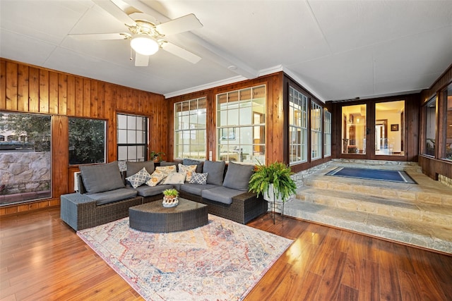 living room with hardwood / wood-style flooring, ceiling fan, and wood walls