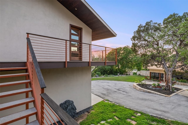 property exterior at dusk with a patio, a balcony, and a yard