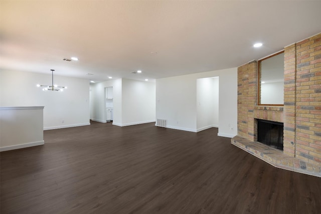 unfurnished living room with a brick fireplace, a notable chandelier, and dark wood-type flooring